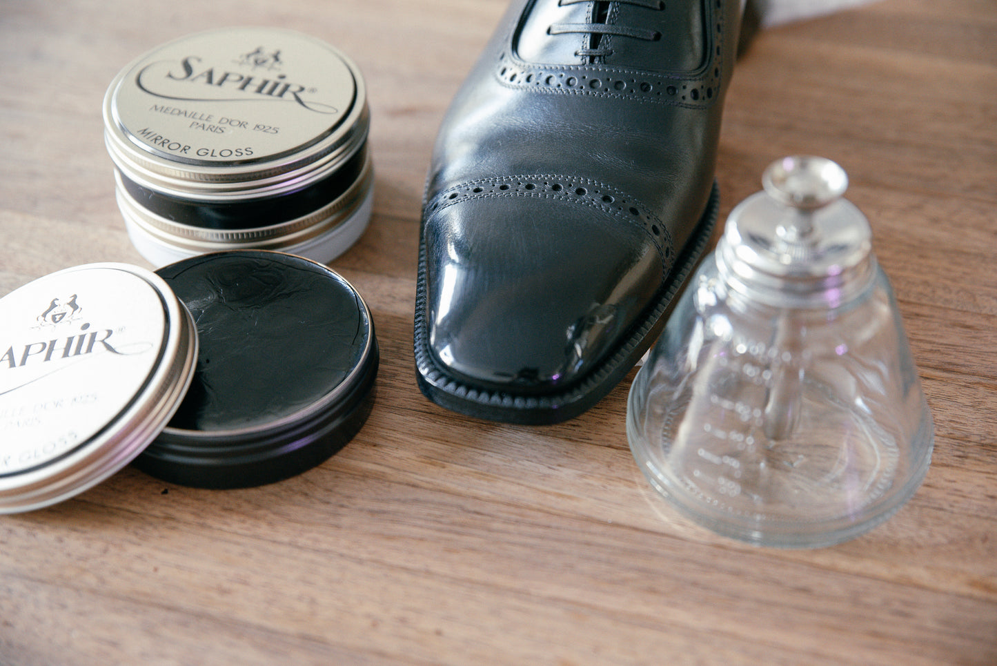Brillaré mirror shine service photo - Black TOM FORD cap toe leather oxford shoes shown with Saphir Medaille d'or Mirror gloss wax polish and brillaré high shine water dispenser displayed