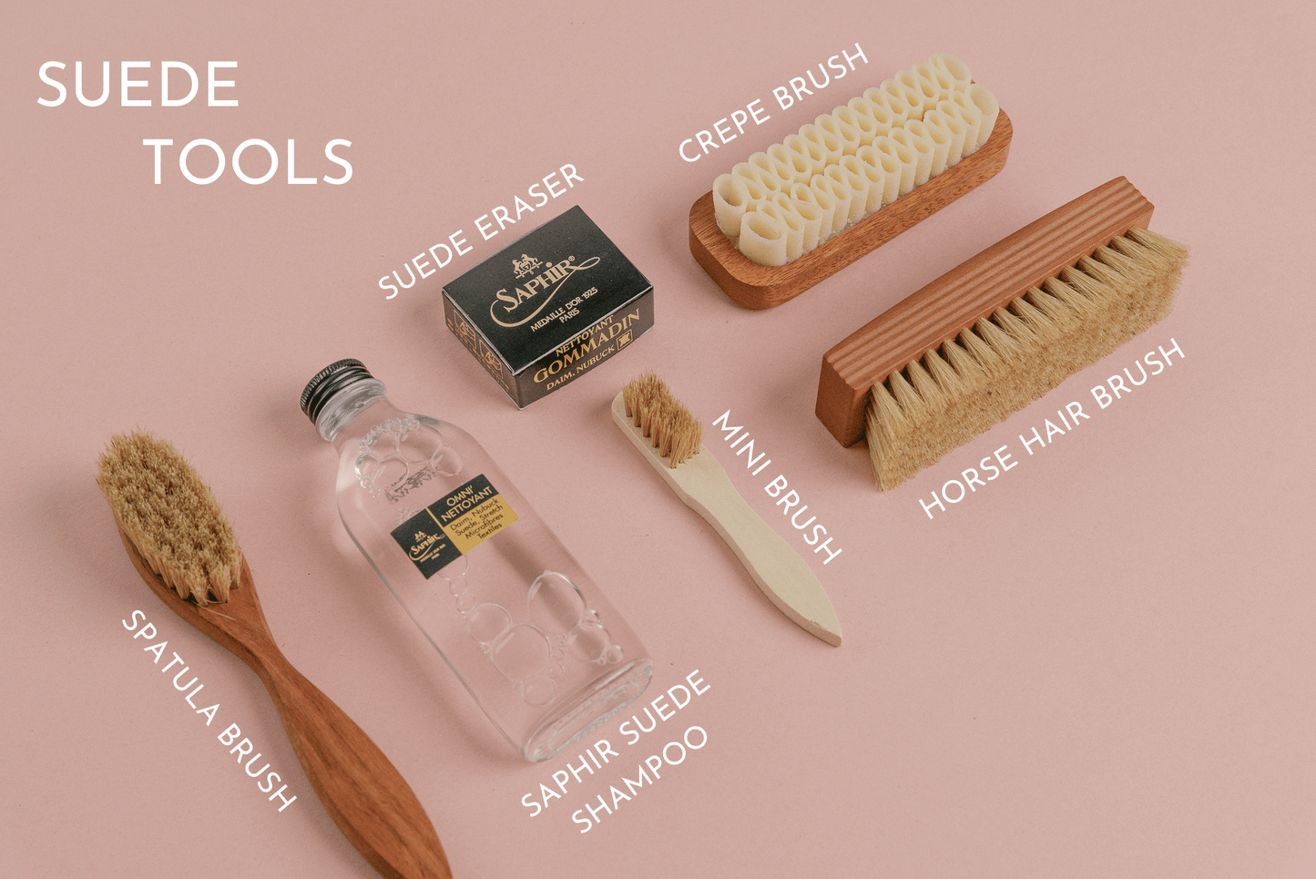 Saphir Medaille d'or omni'nettoyant suede cleaner, suede gommadin brick, and saphir MDO horsehair brush and Saphir Crepe brush shown laid out and labelled on a pink back drop